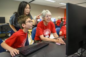A course instructor helps a young boy and his smiling grandmother with their work at a computing station during a Grandparents University social robotics class in the Computer Sciences building at the University of Wisconsin–Madison.